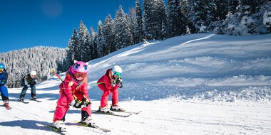 Zwei Kinder fahren in der Hocke mit den Skiern einen Ziehweg entlang und die Elter folgen direkt dahinter | © Salzburger Sportwelt, Christian Schartner