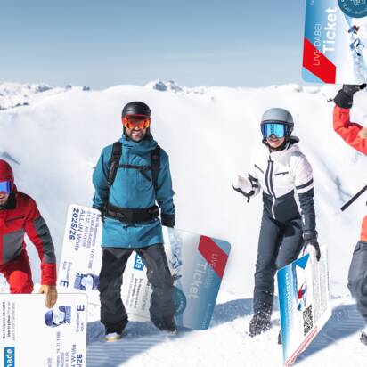 Vier Wintersportler posieren mit übergroßen Skipässen im Schnee vor alpiner Bergkulisse.