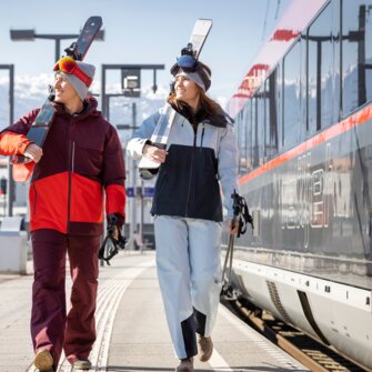 Drei Personen mit Skiausrüstung gehen am Bahnsteig neben dem Zug entlang | © ÖBB | Harald Eisenberger