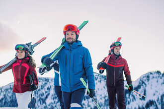 Four skiers carrying their skis on their shoulders – the perfect start for the Back2Ski course, a program for returning skiers. | © Ski amadé