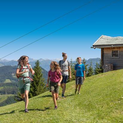 Group of four hikers enjoys a sunny day on the alpine meadow with gondola view and wooden hut in the background in Ski amadé.