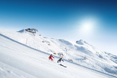 Zwei Skifahrer fahren schwungvoll auf einer frisch präparierten Piste, sonniger Tag | © Ski amadé