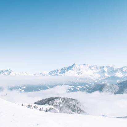 Ein Skifahrer blickt auf verschneite Berge und ein weites Nebelmeer bei klarem Sonnenschein