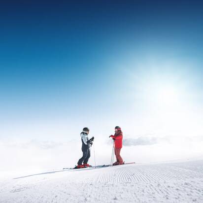 Zwei Skifahrer stehen auf frisch präparierter Piste in Ski amadé mit Blick über wolkenverhangenes Tal