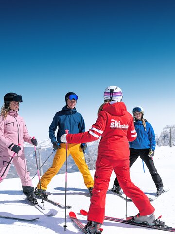 Ski instructor teaches four students in colourful outfits on sunny, snowy slope in Ski amadé