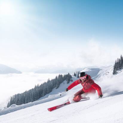 Skier in red suit carves turn on groomed slope with view into the valley in Ski amadé