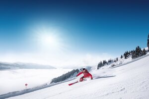 Skifahrer in rotem Anzug fährt sportlich eine Kurve auf präparierter Piste mit Blick ins Tal in Ski amadé