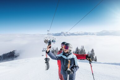 Zwei Skifahrer machen ein Selfie auf sonniger Piste mit Sessellift und Alpenblick in Ski amadé