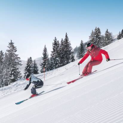 Zwei Skifahrer fahren parallel auf frisch präparierter Skipiste mit Pulverschnee und Sonnenlicht in Ski amadé
