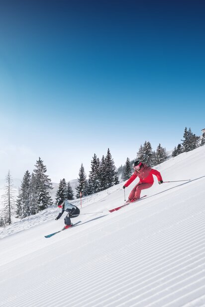 Zwei Skifahrer fahren parallel auf frisch präparierter Skipiste mit Pulverschnee und Sonnenlicht in Ski amadé