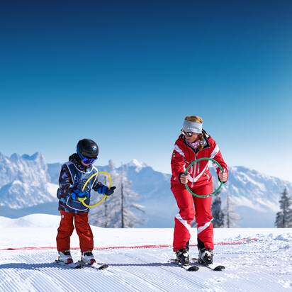 Ski instructor and child practise with coloured rings on sunny slope in the snow at Best Learn2Ski amadé course