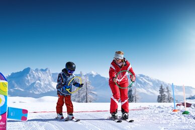 Skilehrerin und Kind mit bunten Ringen üben auf sonniger Piste im Schnee bei Best Learn2Ski amadé Kurs
