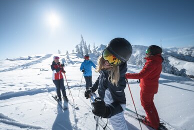 Vier Skifahrer genießen die Sonne auf einer verschneiten Piste. Eine Frau im Vordergrund lacht in die Kamera. | © Ski amadé