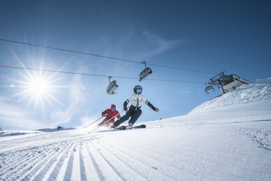 Two skiers carving beneath lift in bright mountain sun