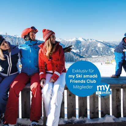 Vier Skifahrer in bunter Winterkleidung sitzen entspannt auf Holzbank vor verschneitem Alpenpanorama.